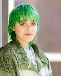 Professional headshot of Ari Forsyth, a white gender non-conforming person in their mid-20s with short green hair