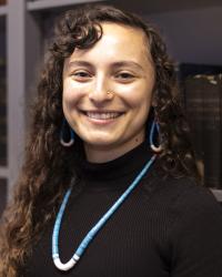 Headshot photo of Sierra Mondragón standing in front of bookshelf